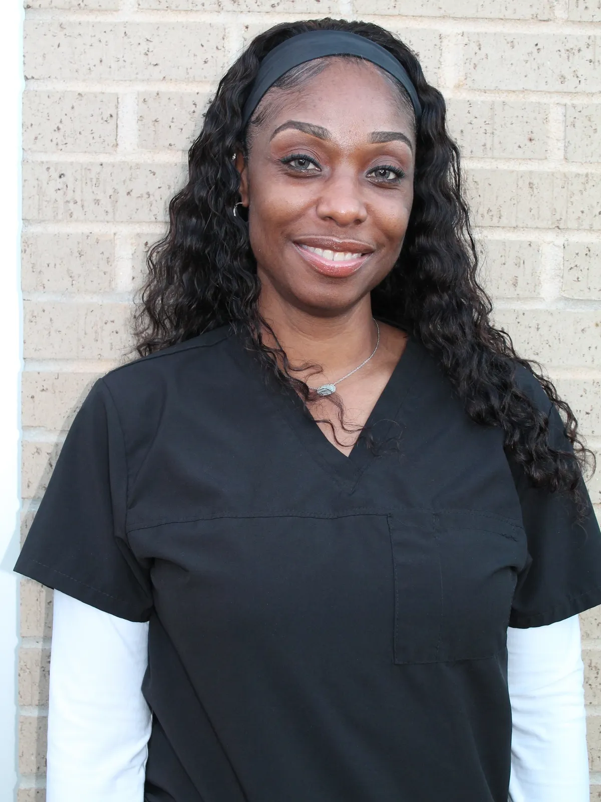 Connie McKinney A woman in black scrubs standing next to a brick wall.